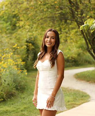 high school senior girl wearing white dress poses amid trees and flowers
