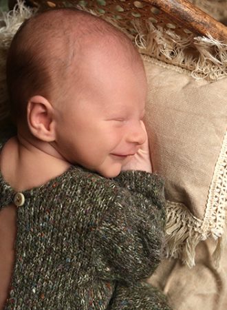 smiling newborn baby wearing green knit romper for photoshoot