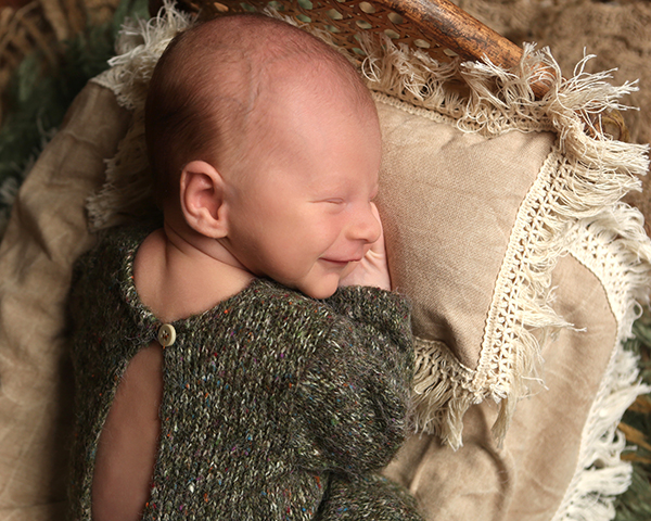 smiling newborn baby wearing green knit romper for photoshoot