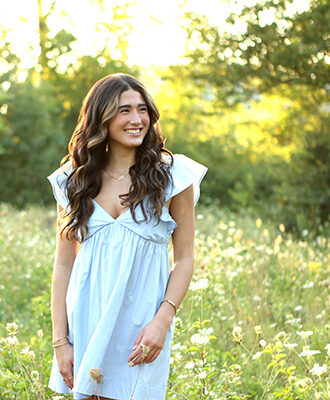 girl giggles while standing in field of flowers wearing a blue dress for senior photoshoot in Carmel