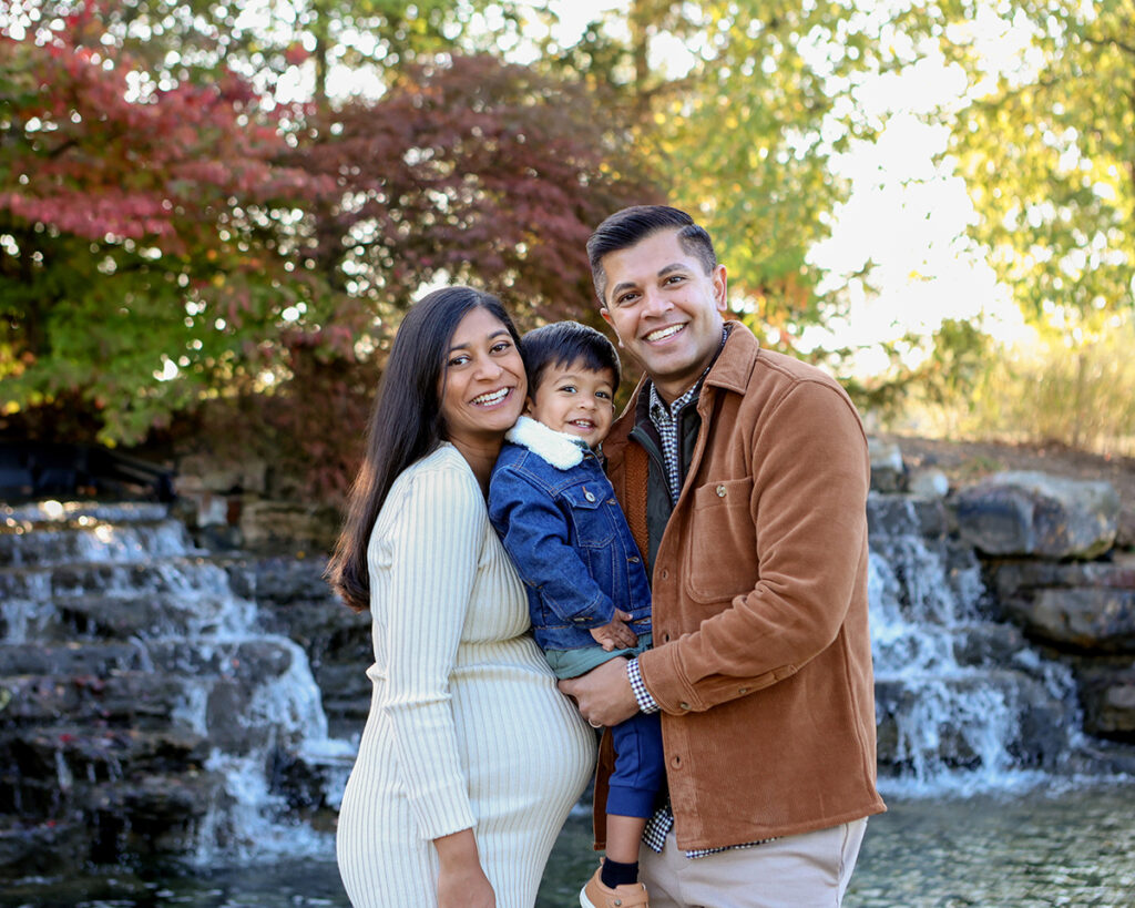 pregnant woman snuggles husband and son at a waterfall at coxhall gardens in carmel