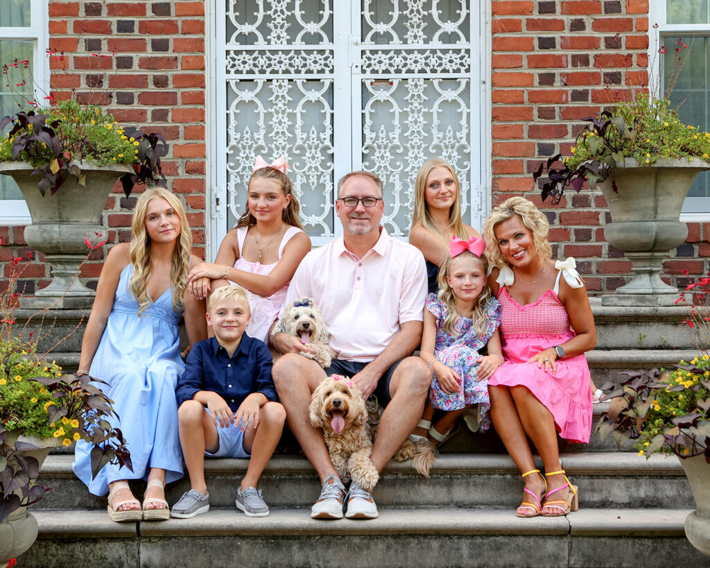 family wearing blue and pink sits on stone steps at coxhall gardens