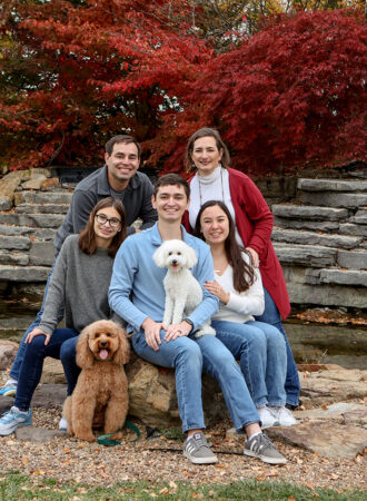 family poses on rocks with dogs for portrait at coxhall gardens