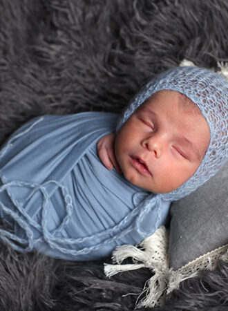 newborn wrapped in blue fabric wearing blue bonnet