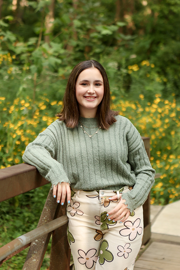 High school senior posing on a rustic wooden bridge surrounded by green trees at Flowing Well Park