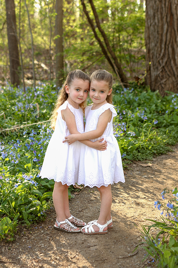 two little girls hug each other in front of the bluebells at carmel's flowing well park
