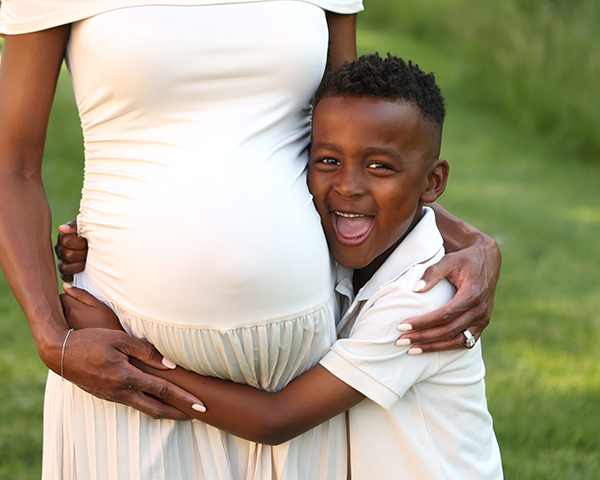 little boy wearing white shirt hugs mom's pregnant belly and laughs