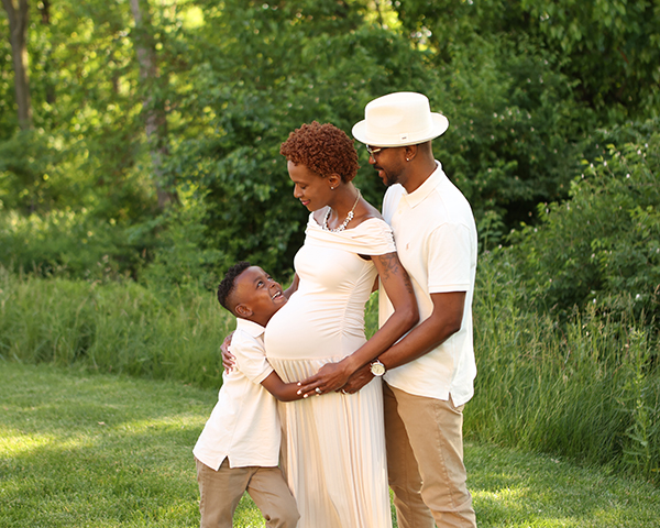 couple smiles at son who snuggles mom's pregnant belly
